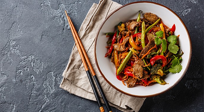 Bowl of stir-fry noodles on a rustic surface with a napkin and chopsticks